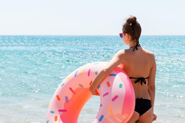 Fille mince à lunettes de soleil tient un anneau en caoutchouc beignet sur la plage au fond de la mer