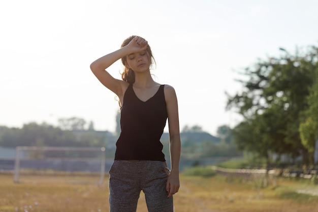 Une fille mince sportive en leggings et en haut est debout avec un tapis d'entraînement, se reposant entre les exercices.