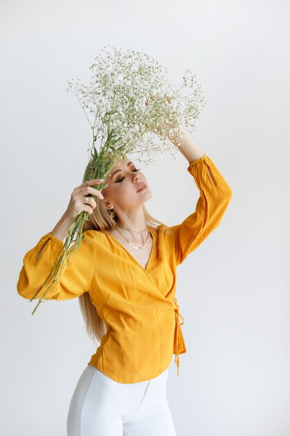 Fille à la mode avec un bouquet de fleurs séchées posant sur un fond clair