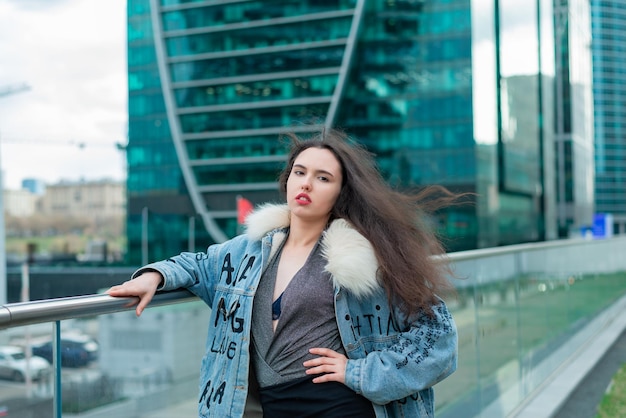 Une fille à la mode avec une coiffure ondulée et des lèvres rouges pose dans la rue