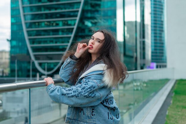 Une fille à la mode avec une coiffure ondulée et des lèvres rouges pose dans la rue