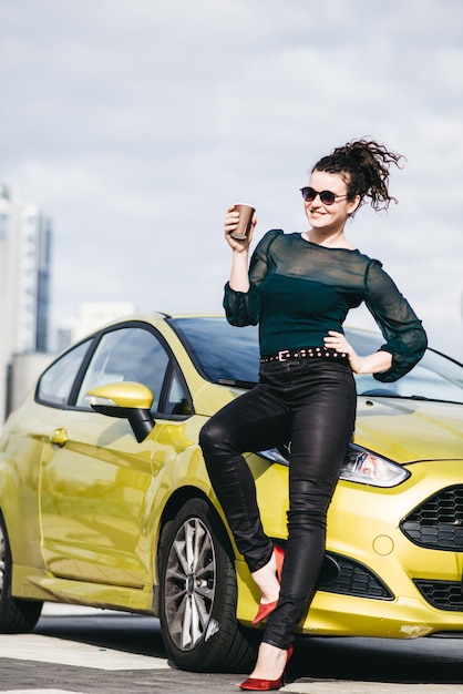 Fille à la mode debout près de sa voiture dans la ville moderne