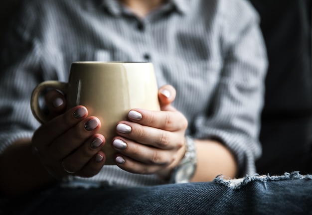 Fille à la mode élégante avec une tasse de café et manucure en jeans. Mode, soins, beauté