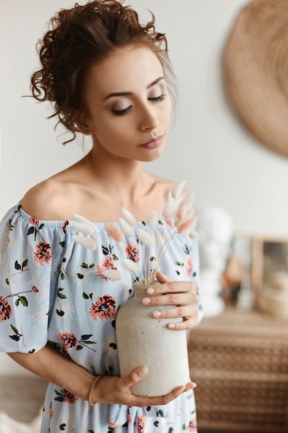 Fille modèle aux cheveux bouclés et corps mince en robe de printemps léger posant à l'intérieur de la maison. Mode d'été