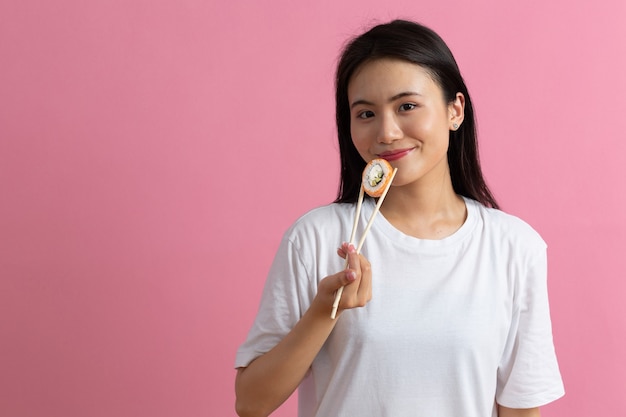 Fille modèle de beauté asiatique mangeant un rouleau de sushi, une cuisine japonaise saine. Belle femme tenant des baguettes avec un rouleau de Philadelphie