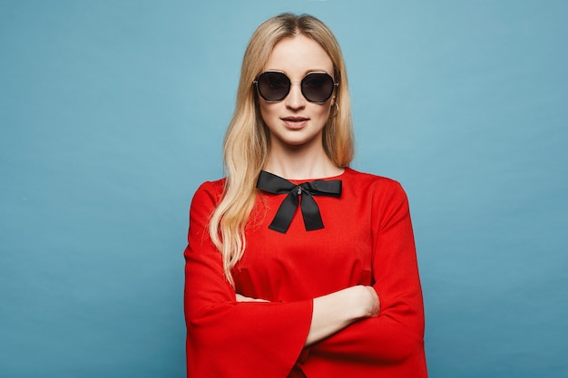 Fille modèle blonde belle et sexy avec un maquillage doux dans des lunettes de soleil élégantes et dans la robe rouge courte à la mode posant, isolé