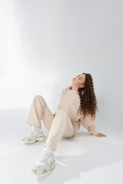 Fille modèle avec une coiffure afro dans des vêtements à la mode et des baskets posant sur fond blanc