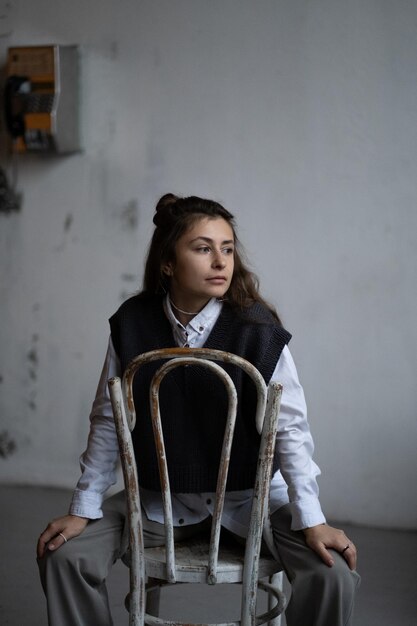 Une fille modèle avec de longs cheveux ondulés sombres pose dans une chemise blanche et un pull gilet en tricot gris