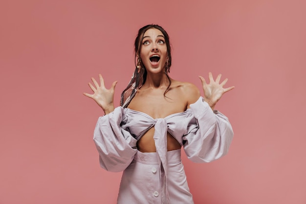 Fille moderne émotionnelle avec une coiffure cool en chemisier à la mode et jupe lilas rayée posant sur fond rose isolé