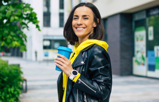 Une fille moderne en promenade! jeune fille moderne, profitant de sa journée, avec une boisson chaude dans sa tasse thermique confortable, avec sa nouvelle jolie montre intelligente.