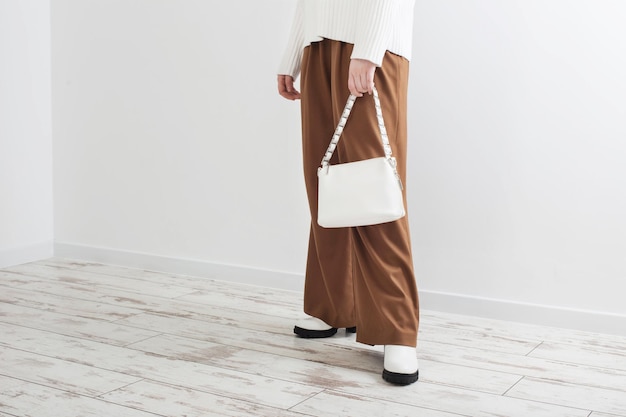 Fille moderne en pull blanc et pantalon marron en salle blanche