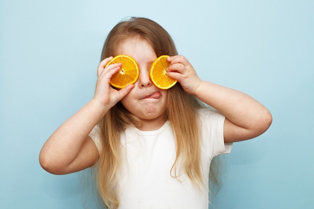 Fille avec des moitiés d'oranges sur fond bleu