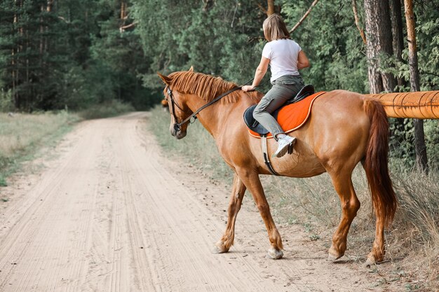 Une fille monte à cheval pendant l'été chaud dans la forêt