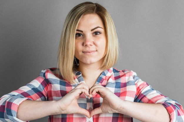 Une fille montre le signe du coeur d'une main sur un fond gris