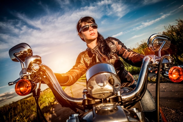 Fille de motard dans une veste en cuir sur une moto en regardant le coucher du soleil. Filtre appliqué en post-production.