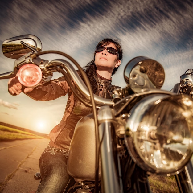 Fille de motard avec des lunettes de soleil se reposant sur la moto