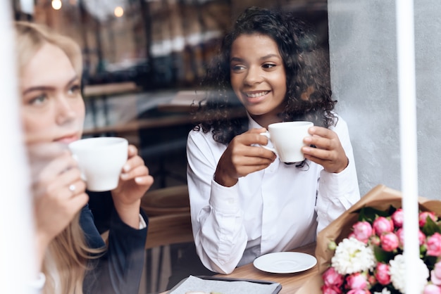 Fille et mulâtre sont assis dans un café et boivent du café.