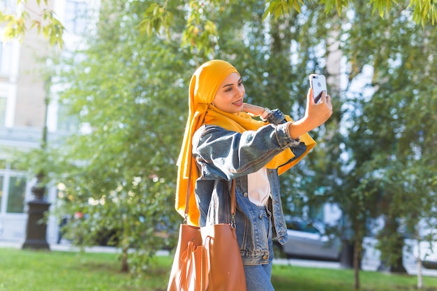 Fille musulmane en hijab fait un selfie au téléphone debout dans la rue de la ville