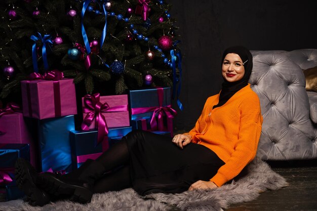 Une fille musulmane en hijab noir rêve d'un cadeau pour les vacances du nouvel an. Célébration de Noël des gens de religion islamique.