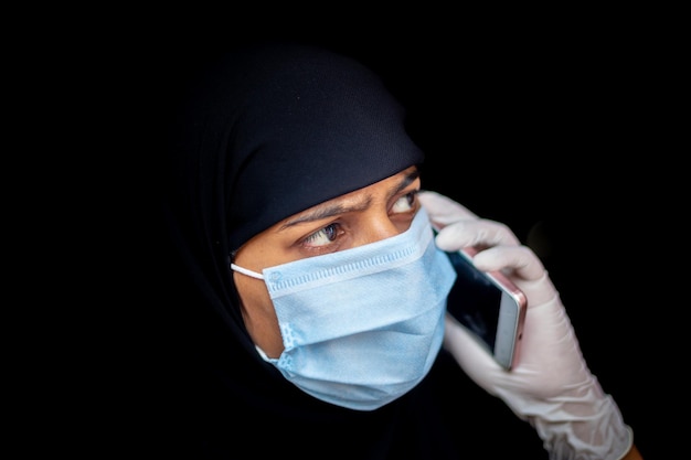 Une fille musulmane portant un masque de sécurité et des gants parle sur son smartphone