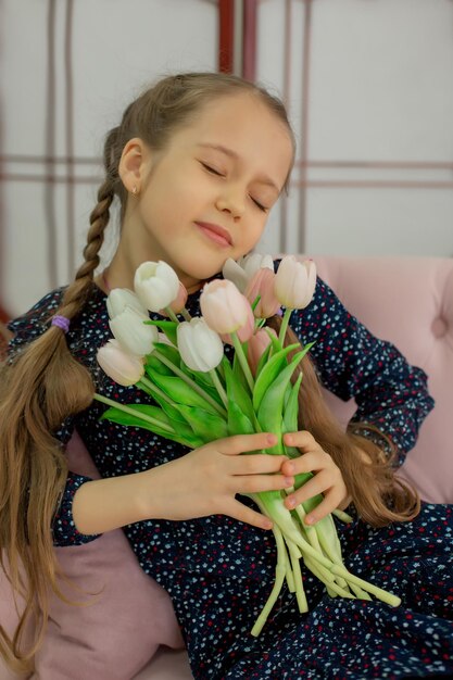 une fille avec des nattes est assise sur un canapé rose avec des tulipes dans les mains