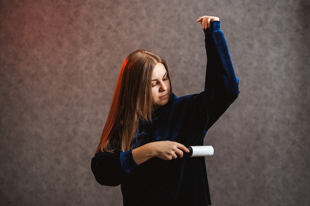 La fille nettoie un chandail avec un rouleau spécial avec du ruban adhésif