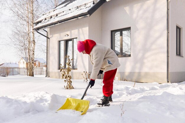 Photo une fille nettoie la neige près de la maison conséquences de la chute de neige