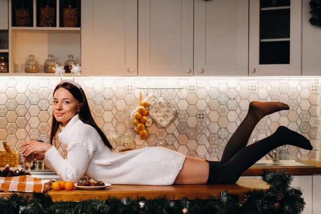 Une fille à Noël est allongée sur la table de la cuisine et tient une coupe de champagne.Femme le soir du nouvel an avec du champagne