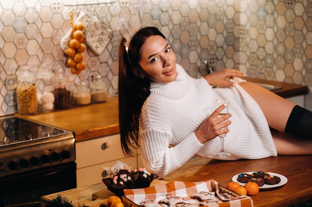 Une fille à Noël est allongée sur la table de la cuisine et tient une coupe de champagne.Femme le soir du nouvel an avec du champagne