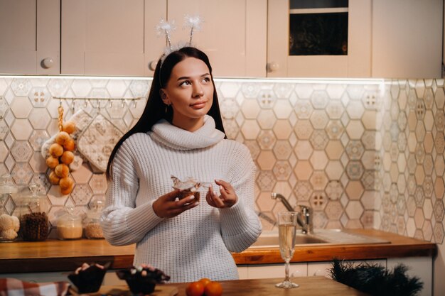 Une fille à Noël se tient dans la cuisine et tient un gâteau dans ses mains et ses rêves. Femme le soir du nouvel an dans la cuisine