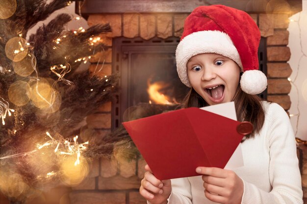 Fille de Noël avec Wow Shock Face s'amusant à recevoir une lettre d'enveloppe de cadeau de Noël