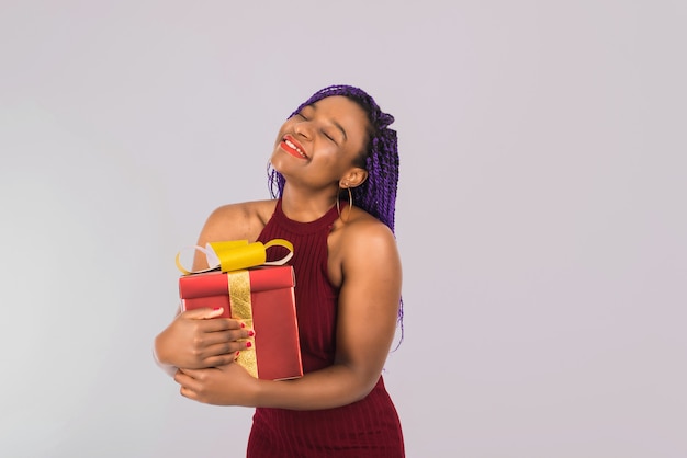 Une fille noire apprécie un gros cadeau de Noël rouge. La fille sourit et reçoit un cadeau. Isolé sur bleu