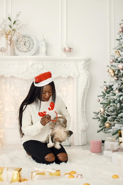 Fille noire au chapeau du père Noël assis près de l'arbre de Noël tenant un petit chien