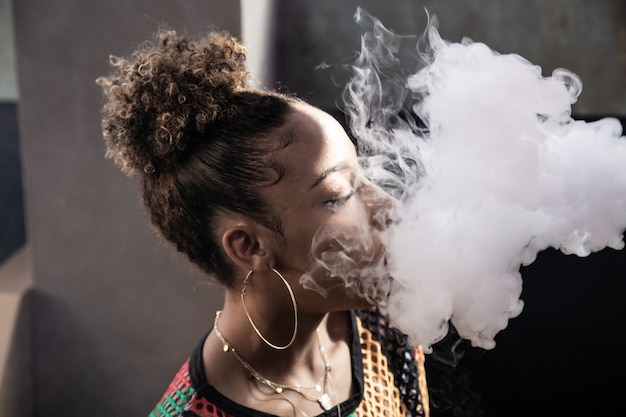 Fille Noire Aux Cheveux Bouclés Et Grandes Boucles D'oreilles Fumant Avec Un Bateau à Vapeur