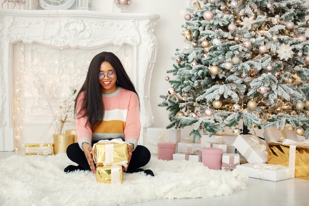 Fille noire à lunettes près du cadeau d'ouverture de l'arbre de Noël à la maison