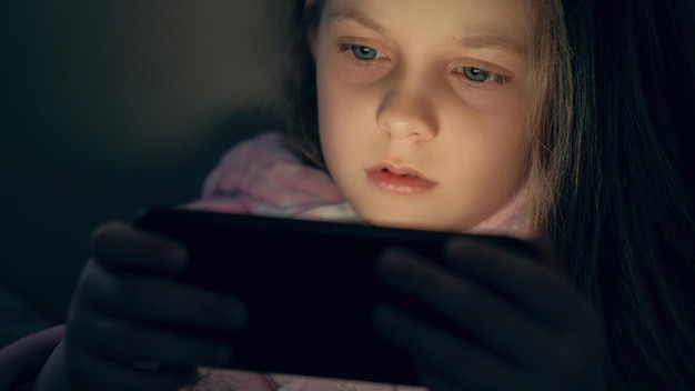 Fille de nuit de gadget enfant regardant la vidéo sur le téléphone