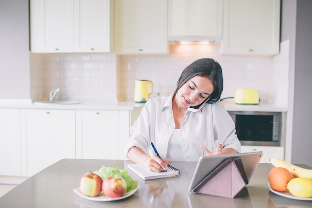 Fille occupée est assise à table et parle au téléphone.