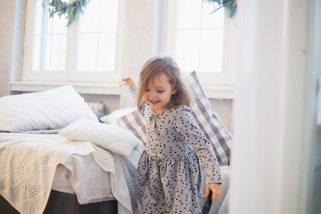 Fille avec un oreiller, les enfants se battent des oreillers sur le lit, la fenêtre décorée d'une couronne de Noël, la vie, l'enfance