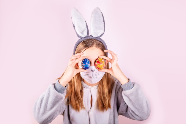 Fille en oreilles de lapin lapin sur la tête et masque de protection avec des oeufs colorés sur fond rose.