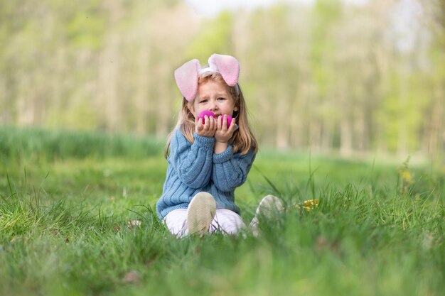 La fille avec des oreilles de lapin rassemble les oeufs dans un panier pour Pâques