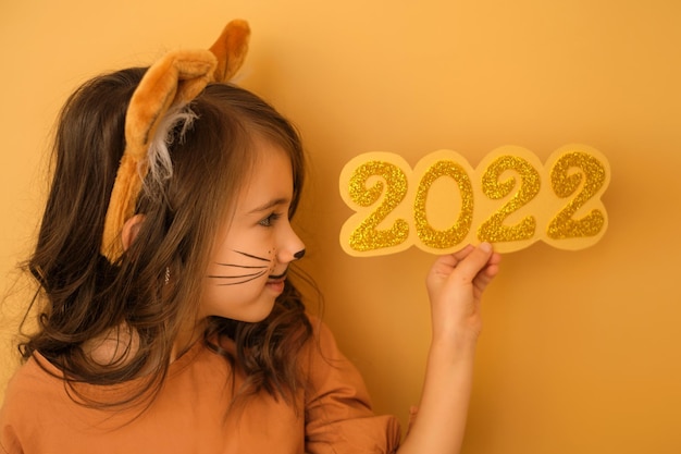Une fille avec des oreilles et un masque aquatique de tigre peint sur son visage tient les chiffres du nouvel an 2022