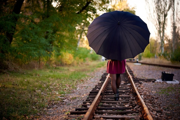 Une fille avec un parapluie noir marche sur le chemin de fer.