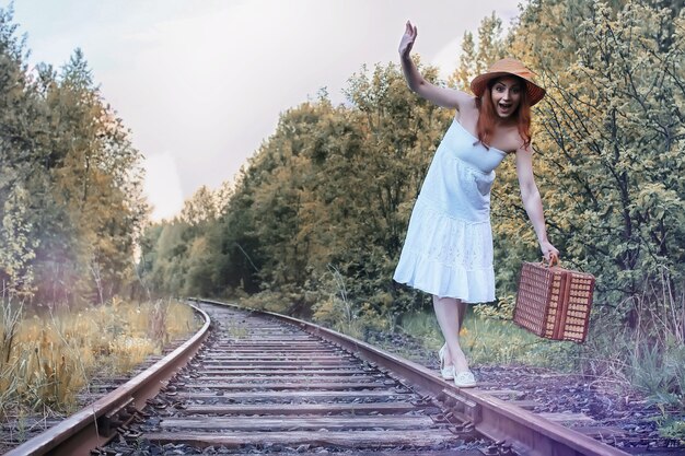 Fille de parc d'automne dans une robe d'été blanche et une valise en osier marchant sur des rails