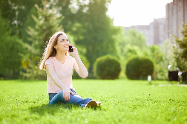 Fille parlant au téléphone assis dans le parc sur l'herbe