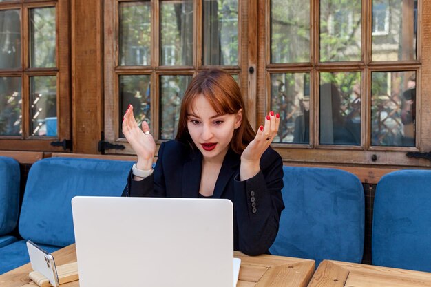 Photo la fille parle sur une liaison vidéo une fille en costume noir parle sur une connexion vidéo sur un ordinateur portable dans un café montrant différentes émotions