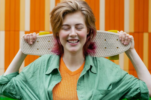 Fille patineuse souriante tenant une mini planche en plastique contre un mur urbain coloré