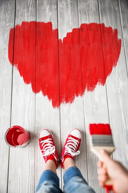 Fille peignant le grand coeur rouge sur le fond en bois. Carte de Saint Valentin heureuse. Concept de rénovation et de design