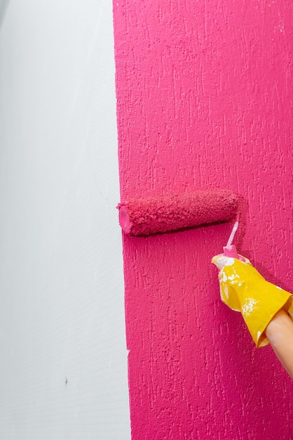 Une fille peint un gros plan de mur avec un rouleau en rose dans son nouvel appartement Rénovation de l'intérieur et d'un nouvel appartement Pendaison de crémaillère et hypothèque souhaitable