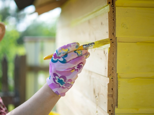 Une fille peint un mur en bois avec un pinceau avec de la peinture jaune