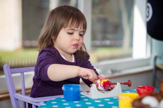 Une fille peint un œuf sur la table à la maison.